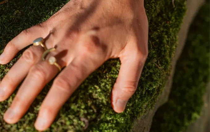 Eine Hand mit Ringen ruht auf bemoostem Boden