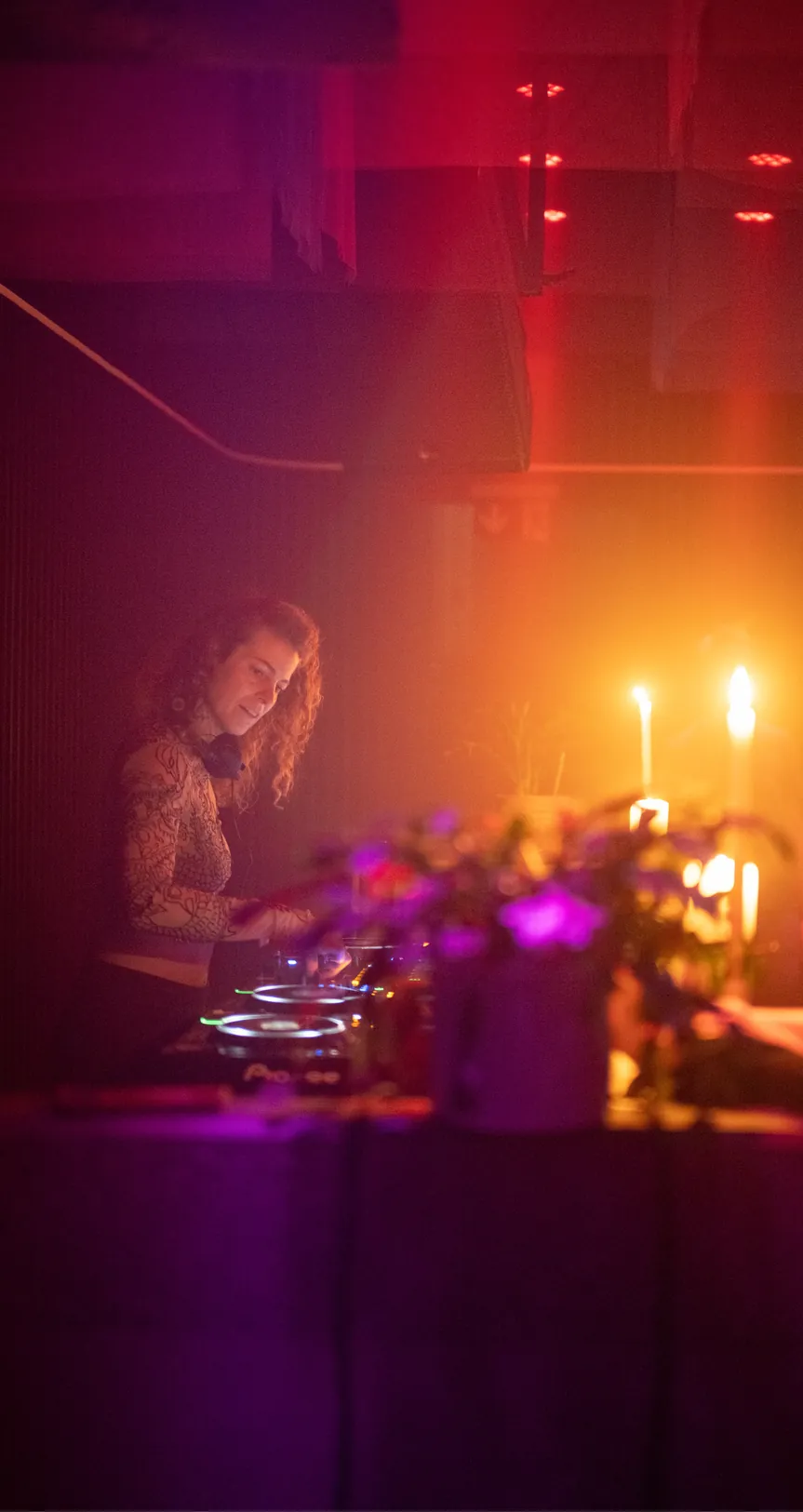 Nora Milena am DJ-Pult, im roten Licht mit Kerzen