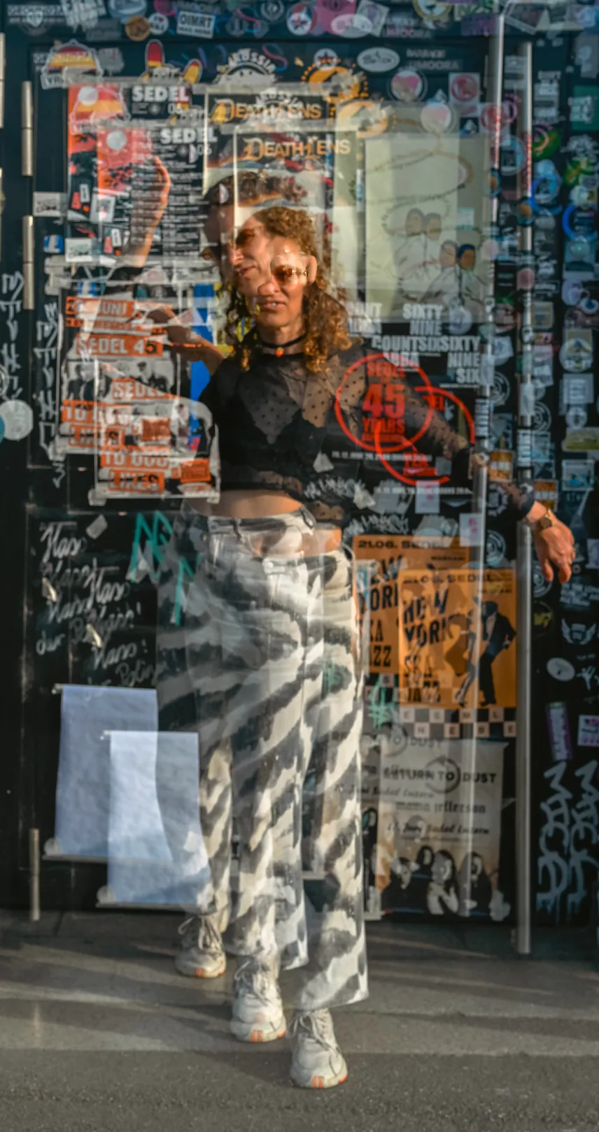 Nora Milena vor einer mit Plakaten und Graffiti beklebten Wand